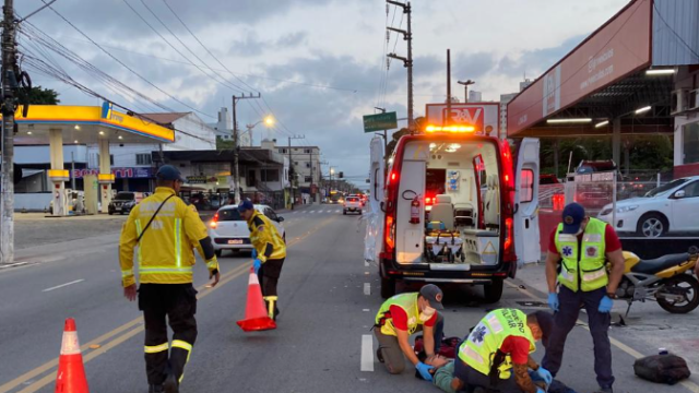 Motociclista caído no chão sendo atendido por equipes de resgate